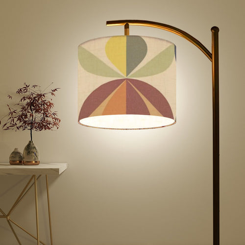 An arc lamp with a drum lampshade and a geometric design on it in greens, yellows, reds, oranges, and cream